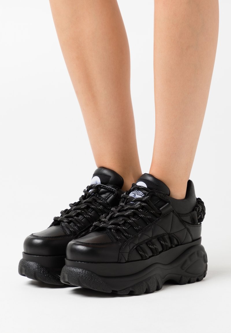 Svarta plattformssneakers har en slät läderöverkappa, texturerade accenter, tjock sula och kontrasterande snörning. Designade för en bekväm passform.