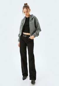 Chaqueta con capucha gris con cierre, puños acanalados, combinada con pantalones negros de rayas y una camiseta corta negra ajustada, completada con botas negras.