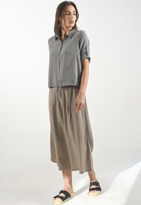Sivá krátkozrná button-up košeľa s sťahovacím lemom, doplnená o béžovú, voľne padnúcu, midi dĺžku sukne a čierne šľapky.