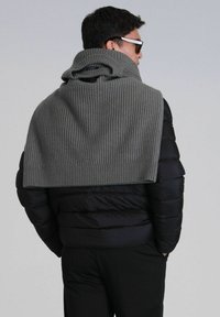 Châle à col ch�âtaigne en tricot côtelé gris drapé sur une doudoune noire. Texture remarquable et design superposé visibles, mettant en avant la chaleur et le confort.
