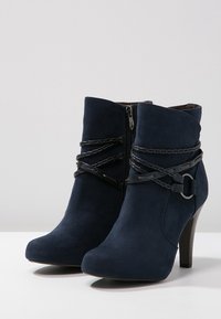 Marinblå suedesneakers med rund tå, hög klack och dekorativ svart kedjedetalj runt ankeln, med en sidoglidare.