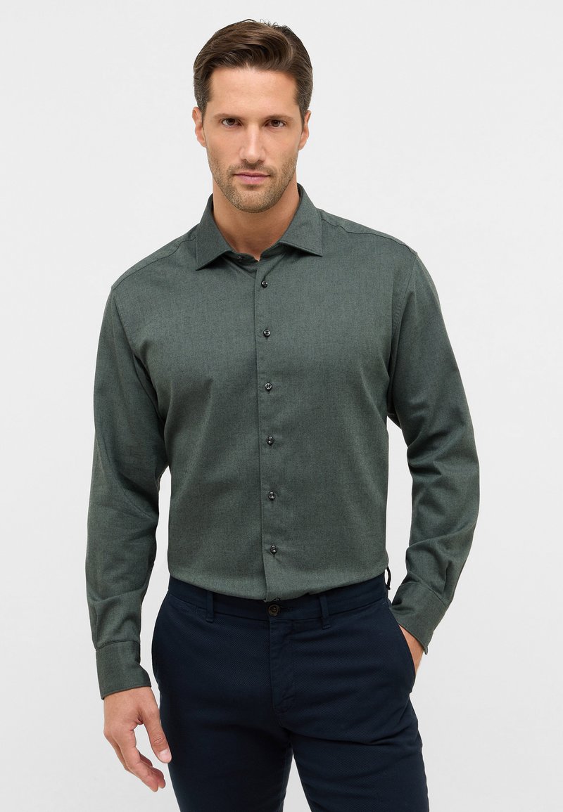 Camicia botton-up verde scuro con tessuto texture, maniche lunghe, colletto a punta e bottoni neri, abbinata a pantaloni blu navy.