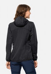 Svart softshell-jakke med en tilpasset design, hette og elastiske mansjetter. Har en teksturert overflate og en diskré logo nær sømmen.
