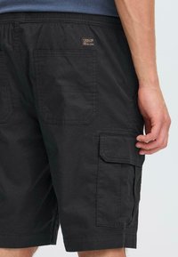 Shorts cargo noirs en tissu durable, dotés de plusieurs poches, d'un logo brodé et d'une coupe décontractée. Design uni sans motifs.