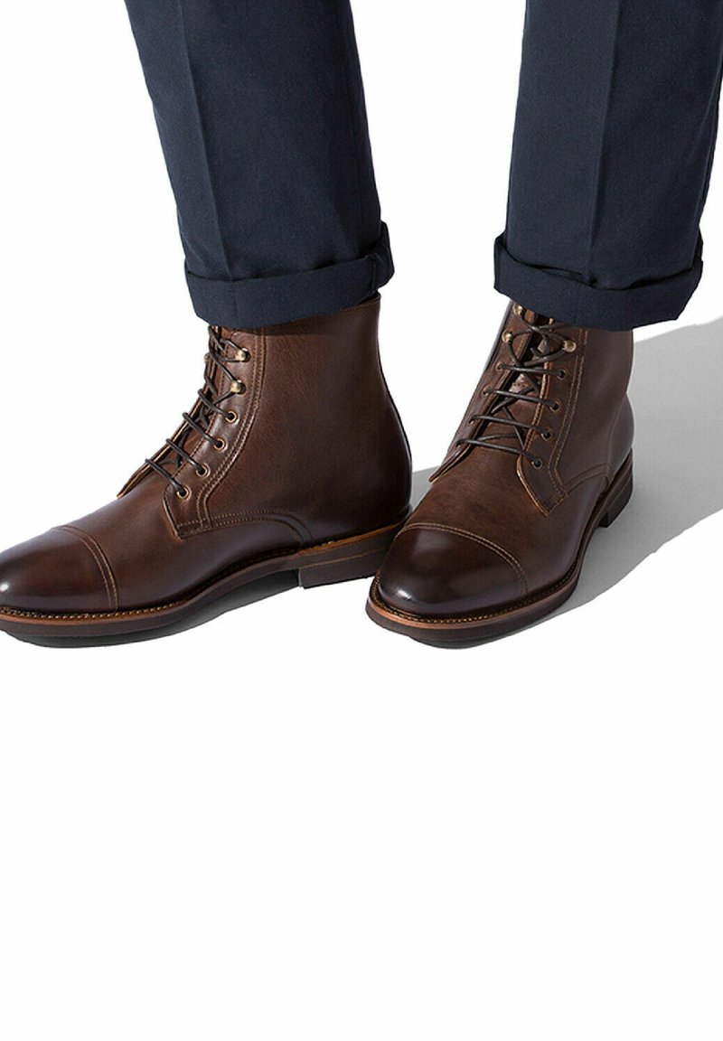 Stivali alla caviglia in pelle marrone con texture liscia, design a punta rinforzata e chiusura con lacci. Suola robusta con una leggera lucentezza e cuciture a contrasto.