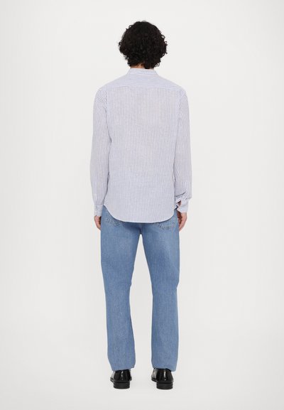 Dolga majica z belimi in modrimi črtami, kombinirana s svetlomodrimi kavbojkami. Majica ima ovratnik in ukrivljeno spodnje rob, z manšetami na gumb.