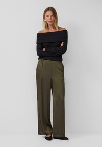 Schwarzer, strukturiert off-shoulder Pullover kombiniert mit olivgrünen, satinierten, weiten Hosen und schwarzen, spitzen Ballerinas.