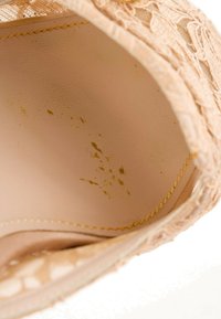 Gros plan de l'intérieur beige de la chaussure montrant le bord en tissu texturé, la couture jaune et plusieurs petites taches sombres sur la semelle intérieure.