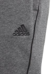 Grå sportsbukser lavet af blødt stof med en tekstureret overflade, med et syet sort Adidas-logo på venstre side.