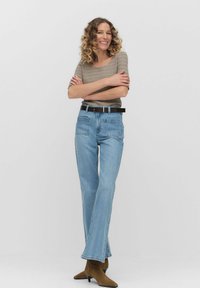 Vaaleansiniset leveälahkeiset farkut, joissa on kaksi takataskua, yhdistettynä beige raidalliseen lyhythihaiseen paitaan ja mustaan vyöhön. Nubukka ruskeat nilkkurit.