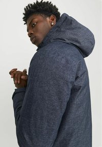 Chaqueta con capucha para hombre de color azul oscuro, texturizada, con un cuello alto y puños elásticos. Presenta una cremallera frontal y un diseño minimalista.