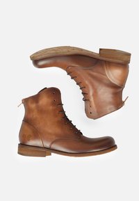 Botas de cuero marrón hasta el tobillo con puntera redondeada, cierre de cordones y cremallera, superficie texturizada y suela de madera con un pequeño tacón.