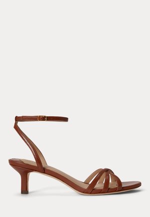 Brązowy skórzany sandał na niskim obcasie z trzema paskami z przodu i regulowanym paskiem wokół kostki z złotą klamrą.