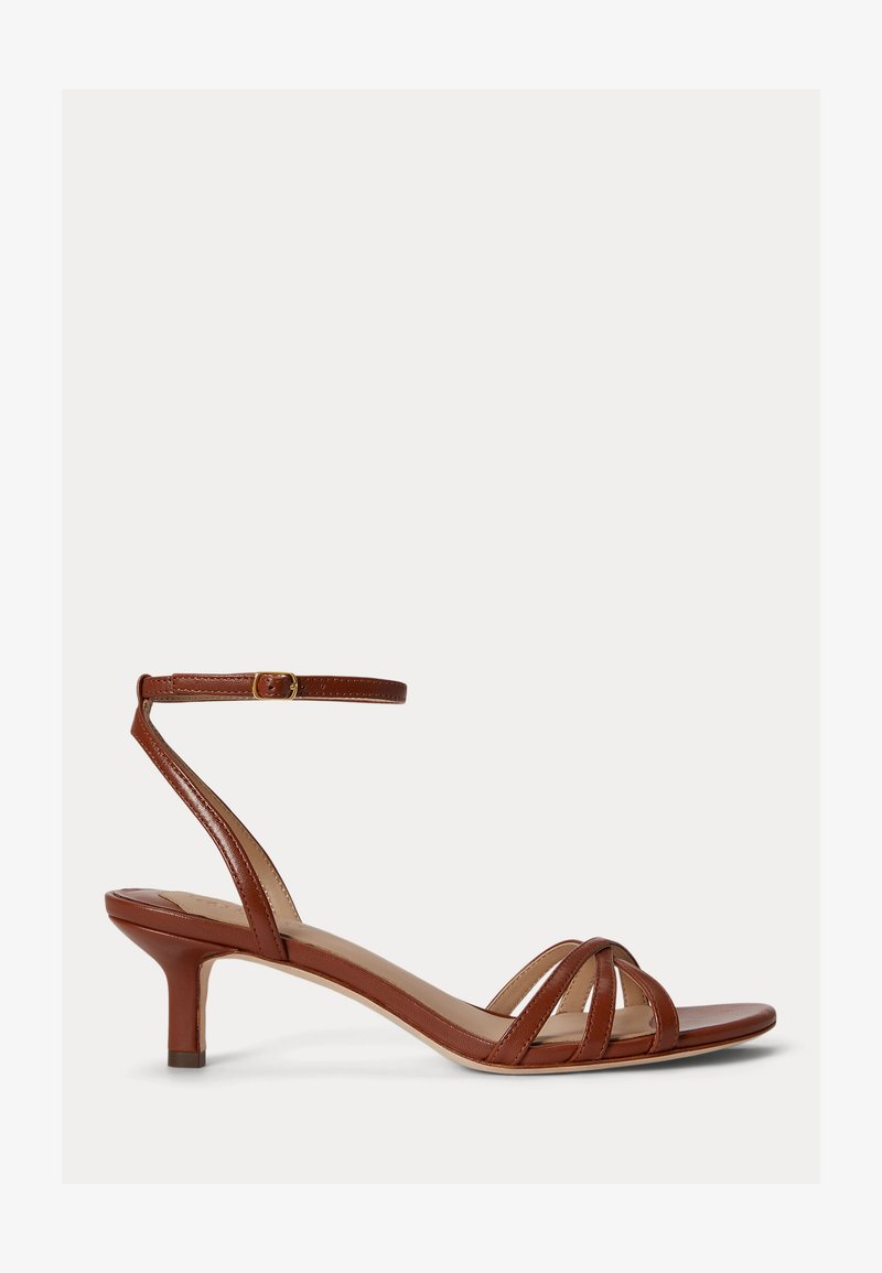 Καφέ δερμάτινο σανδάλι με χαμηλό τακούνι, τρεις λουράκια μπροστά και ρυθμιζόμενο λουρί στον αστράγαλο με χρυσή αγκράφα.