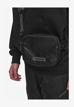 Crni najlon torba preko tijela pravokutnog oblika, sa zatvaranjem na zip i brendiranim komadom. Ima čvrstu podesivu naramenicu i glatku teksturu.