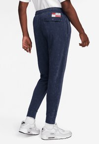 Dunkelblaue Jogginghosen aus strukturiertem Stoff, mit elastischem Bund und einer einzelnen Gesäßtasche mit einem Logo-Patch. Mit einer schlanken Passform akzentuiert.