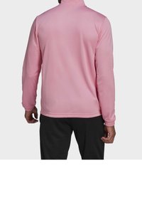 Rosa träningsjacka med dragkedja, lång ärm och hög krage. Har elastiska ärmslut och är tillverkad av ett mjukt, lätt material.