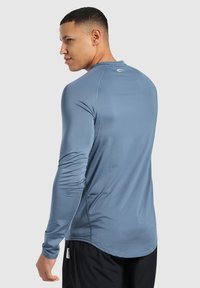 Langärmliges Sportshirt in Hellblau, aus dehnbarem Stoff gefertigt. Verfügt über einen Rundhalsausschnitt und Akzentnähte entlang der Nähte.