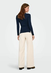 Granatowa koszula z długim rękawem o dopasowanym kroju, zestawiona z kremowymi spodniami o szerokich nogawkach. Tkanina wydaje się miękka i gładka w dotyku.