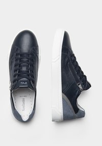 Baskets en cuir bleu marine avec des semelles en caoutchouc blanc, dotées d'une fermeture à zip et d'un design à lacets. Accents en daim gris au talon.