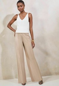 Top in tessuto a costine bianche con scollatura a V abbinato a pantaloni beige a gamba larga. I pantaloni presentano dettagli di cuciture verticali. Tacchi con stampa pitonata completano l'outfit.