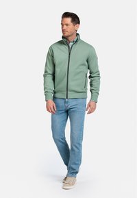 Groene zip-up jas met een hoge kraag, geribbelde manchetten en zijzakken. Draag het met lichtblauwe jeans en beige sneakers.