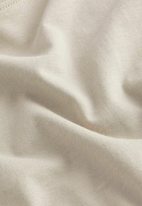 Telig bej deschis cu o textură netedă, având nervuri fine și o ușoară elasticitate, punând în evidență plieri și drapaje moi.
