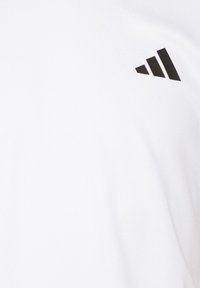 Camiseta deportiva blanca con un acabado texturizado y un logo triangular negro en la parte superior izquierda.