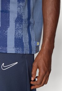 Blå atletisk skjorte med teksturerede lodrette striber; har et logo pålappe og et kontrast Nike-symbol i hvidt på marineblå shorts.