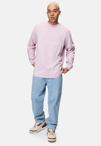 Ljusrosa långärmad sweatshirt med rund hals, tillsammans med ljusblå löst sittande jeans och beige sneakers med bruna detaljer.