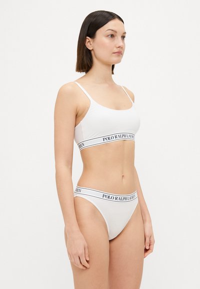 White cotton bralette and matching thong swimwear featuring thin straps and a black logo waistband. Smooth texture with minimal design.