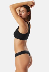 Ensemble de soutien-gorge et de string noir en tissu lisse. Le soutien-gorge a des bretelles larges et un design ajusté. La taille présente un logo texturé subtil.
