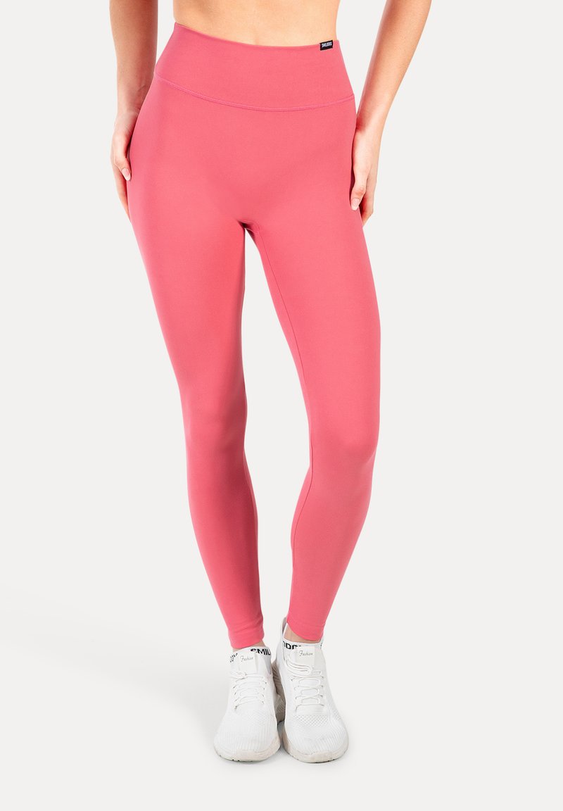 Leggings rosa a vita alta realizzati in tessuto elastico, con una texture liscia e un design aderente, abbinati a scarpe da ginnastica bianche.