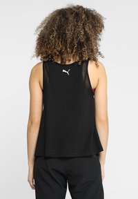 Svart ärmlös linne i mjukt tyg, med en lös passform, nätdetaljer på axlarna och en liten vit logotyp på baksidan.