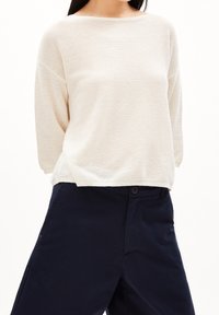 Ljus beige stickad tröja med vid halsringning och trekvartsärmar, i kombination med marinblå strukturerade byxor med knäppning.