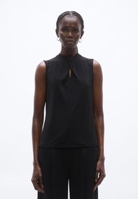 Fekete, ujjatlan felső magas gallérral és kulcslyuk részlettel az elején. Simább anyag, szabott fazon, fekete nadrággal párosítva.