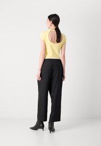 Haut jaune à manches courtes avec une découpure circulaire dans le dos, associé à un pantalon noir taille haute et des bottes à talons noires.