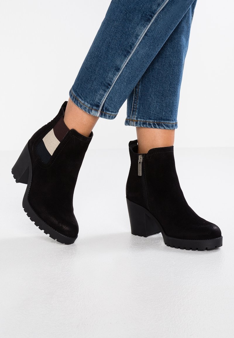 Bottines en daim noir avec un talon épais et une semelle en caoutchouc texturé. Présentent une fermeture éclair et des accents élastiques de couleurs variées.