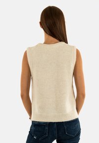 Maglione senza maniche color crema con scollatura e orlo a coste, realizzato in un materiale morbido e texturizzato, esposto su uno sfondo semplice.