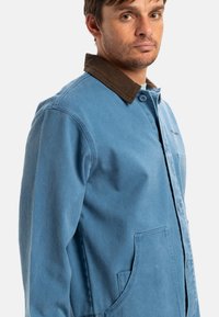 Light blue jacket with a brown corduroy collar, featuring a front button closure and side pockets. Made of durable fabric, showing a textured finish.