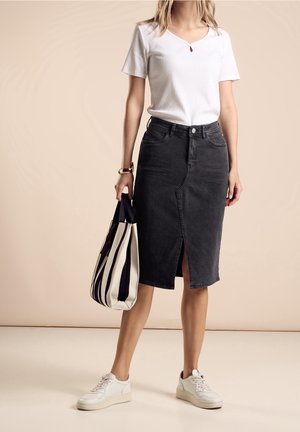 Falda lápiz de mezclilla gris con abertura frontal, combinada con una camiseta blanca de canalé y zapatillas deportivas. La modelo sostiene un bolso tote a rayas.