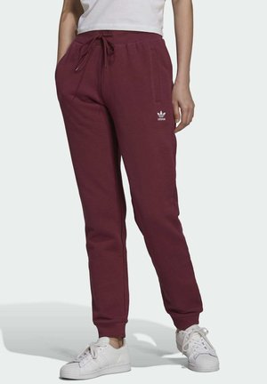 Pantalones de chándal burdeos con cintura elástica y cordón, con bolsillos laterales y un logo blanco. Combinados con zapatillas blancas.