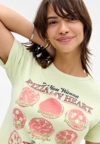 Light green cotton t-shirt featuring a graphic of six pizza varieties in pink and red, with text "If You Wanna PIZZA MY HEART."