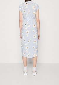 Ljusblå midi-klänning med korta ärmar, prydd med ett blommönster i vitt och gult. Knyten vid midjan, tillsammans med vita sneakers.