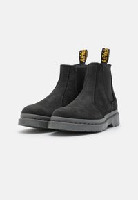 Bottes Chelsea en suede noir avec une tige texturée, des panneaux latéraux élastiques, des languettes jaunes et une semelle en caoutchouc gris avec des détails en relief.