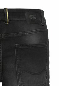 Schwarze Jeans aus Denim mit geradem Schnitt, ausgestattet mit einem gelben Akzent am Bund und einem schwarzen Patch-Label auf der Rückseite. Zwei hintere Taschen sind sichtbar.