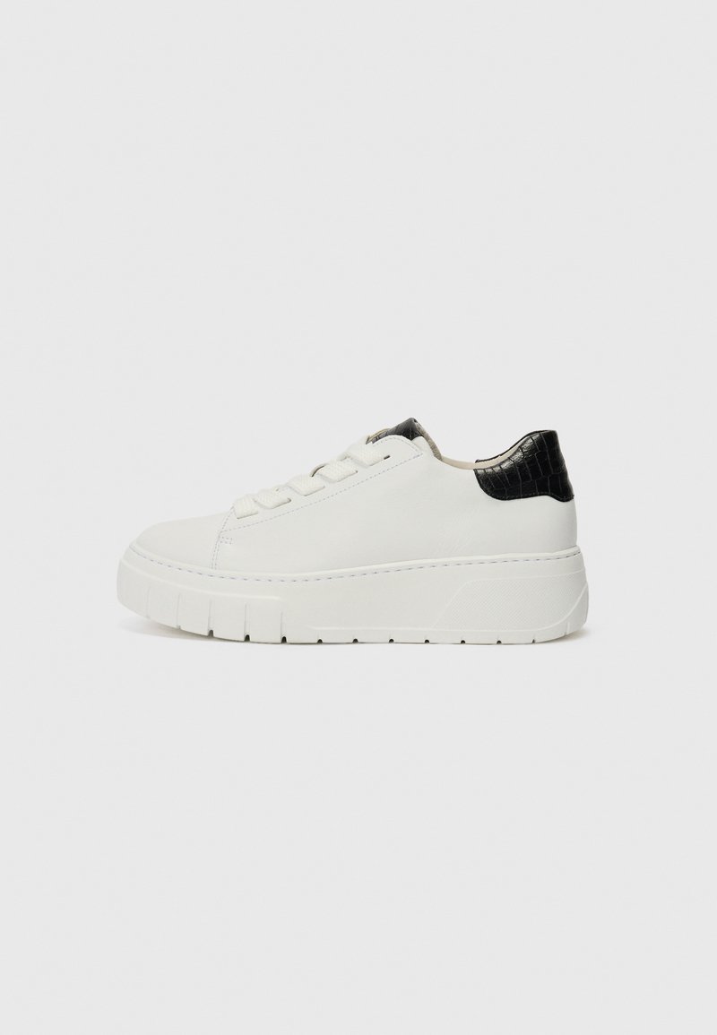 White leather sneaker with a textured black heel accent, rounded toe, and thick white sole featuring horizontal grooves. Simple lace-up design.