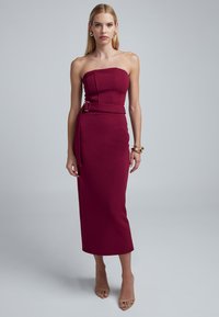 Burgundy kynhittu mekko, jossa on rakenteellinen yläosa ja sivu vyöyksityiskohta. Silkkinen, teksturoitu kangas; polvipituinen; yhdistetty alastomiin korkokenkiin.
