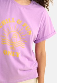 T-shirt en coton violet avec un texte graphique jaune "CHILL & FUN ONLY" accompagné d'un design de verre à cocktail et de soleil, à manches courtes et à coupe décontractée.