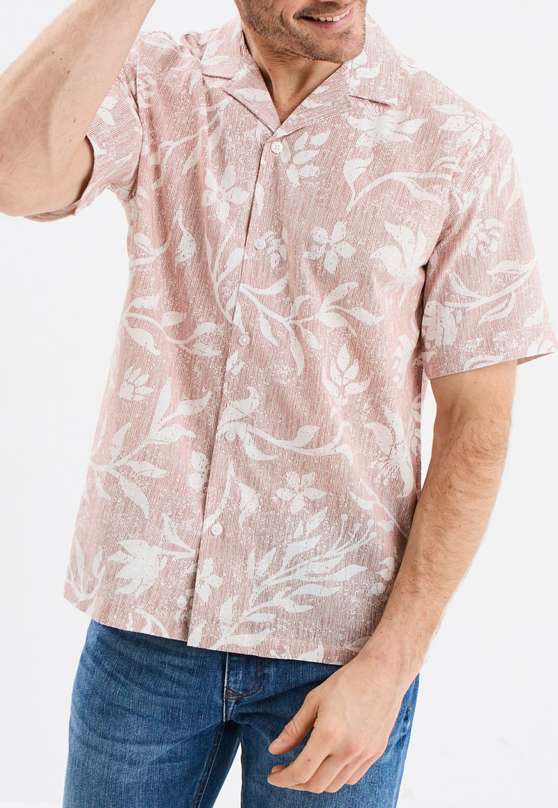 Camisa de botones de manga corta en rosa claro con patrones florales blancos y un acabado texturizado. Presenta un cuello clásico y botones en la parte delantera.